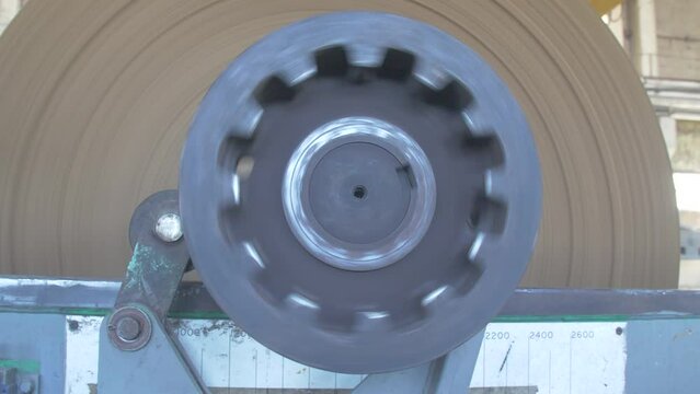 Bobbin of brown paper for making pulp cardboard boxes is spun on an industrial machine. Paper and pulp mill processes a huge sheet of paper
