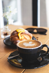 Coffee prepared by a barista in a black cup on a restaurant table. Food accompanying the coffee. Breakfast. Beginning of the day.
