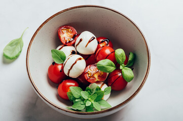 Classic italian salad caprese served in original form with cherry tomatoes, mini mozarella pearls, basil leaves and balsamic glaze