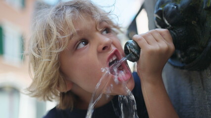 One blond child drinking from public water fountain. Kid drinks from urban street faucet