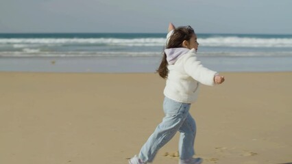 Adorable little girl running to dad and falling into his arms while having fun at seashore on warm autumn day. Man sitting on haunches and hugging his dearest kid with affection. Love, family concept