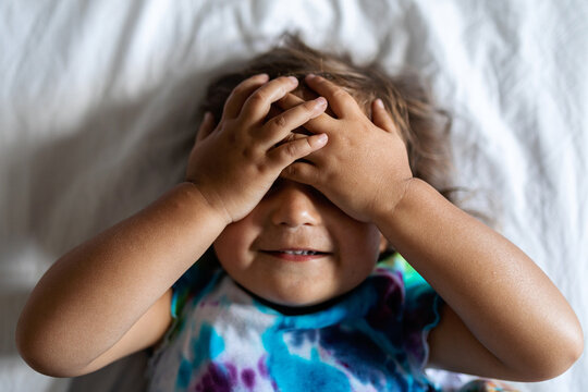 Little girl covering her face portrait on bed