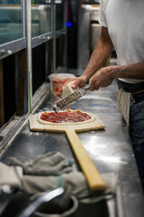 Close up of the making process, male hands rubbed cheese grated. Prepared uncooked raw making pizza Margherita plant-based, with tomato sauce, mozzarella, and basil leaves on a board.