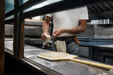 Close up of the making process, male hands rubbed cheese grated. Prepared uncooked raw making pizza Margherita plant-based, with tomato sauce, mozzarella, and basil leaves on a board.