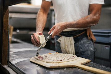 Close up of the making process, male hands rubbed cheese grated. Prepared uncooked raw making pizza...