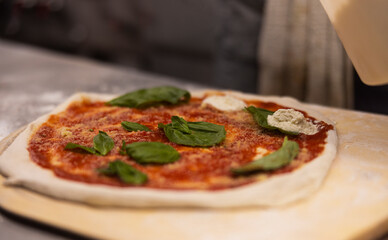 Prepared uncooked raw making pizza Margherita plant-based, with tomato sauce, mozzarella, and basil leaves on a board, close up of making process. 