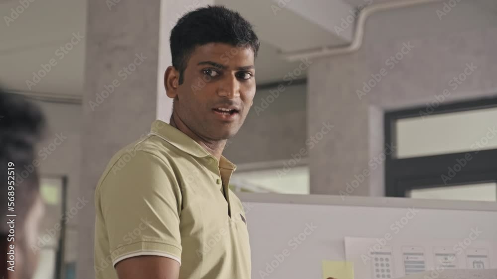 Sticker over the shoulder shot of indian mobile app developer standing by flipchart in office and discussing