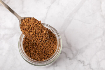 Instant coffee in a spoon. Coffee in granules on a white marble background.Energy hot drink. Place for text. Place for copy. Cheerful morning concept.