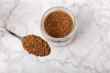 Instant coffee in a spoon. Coffee in granules on a white marble background.Energy hot drink. Place for text. Place for copy. Cheerful morning concept.