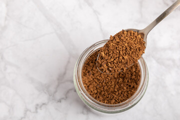 Instant coffee in a spoon. Coffee in granules on a white marble background.Energy hot drink. Place for text. Place for copy. Cheerful morning concept.