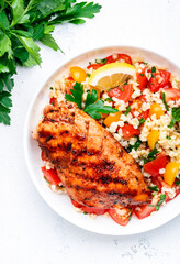 Grilled chicken breast fillet with tabbouleh salad with bulgur, tomato and parsley with lemon dressing, white table background, top view