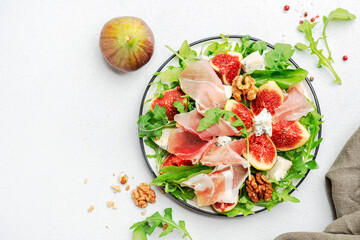 Delicious fig salad with prosciutto, gorgonzola cheese, walnuts, arugula on white kitchen table background, top view