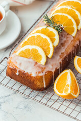 Loaf of orange bread covered with a confectionery glaze with lemon juice and decorated with orange slices. Chiffon cake on a pastry grill next to cup of tea. White background