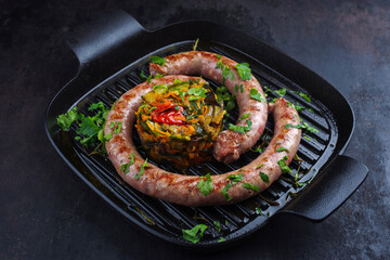 Traditionell gebratene italienische Fleischwurst Salsiccia fresco mit Gemüsetartar und Koriander serviert als close-up in einer gusseisernen Pfanne 