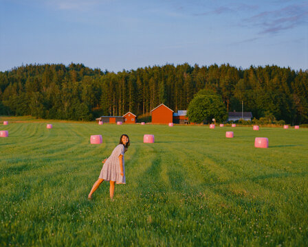 Woman standing on  the field among pink balls of hay