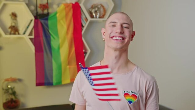 cheerful young man waving the USA flag and showing thumb up, LGBT flag on the shelves, LGBT concept medium closeup. High quality 4k footage