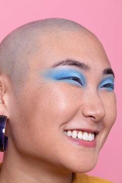 Stylish Asian woman with colorful makeup in front of pink background