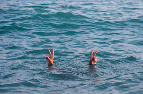 Hands showing peace sign sticking out of the sea depths.