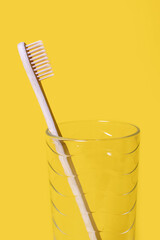 Ecological bamboo toothbrush in a glass cup on a yellow background. Oral hygiene care concept. Environmentally friendly wooden toothbrush