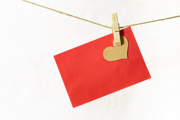 A wooden clothespin is holding a brown heart and a red sheet on a hemp cord. The background is white.