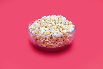 Popcorn in a large glass bowl on a pink background in the center of the image. Crispy classic popcorn snack for watching movies and series. Delicious snack for spending free time and watching TV