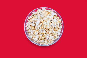 Popcorn in a large glass bowl on a red background in the center of the image. Crispy classic...
