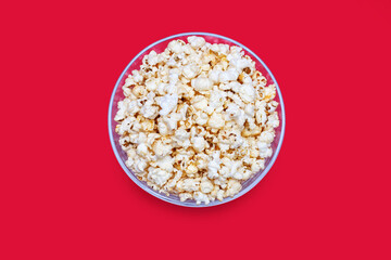 Popcorn in a large glass bowl on a red background in the center of the image. Crispy classic popcorn snack for watching movies and series. Delicious snack for spending free time and watching TV