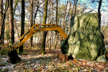 Excavator left in woodland and covered in tarpaulin for snow protection
