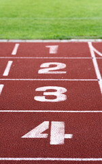 Red running racetrack finishing line with numbers 1-4. Green grass. Vertical photo.