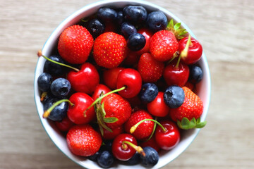 Bowl filled with fresh blueberries, cherries and strawberries on wooden table. Top view. 