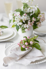 Fototapeta na wymiar Beautiful table decor for a wedding dinner with a spring blooming apple tree flowers. Celebration of a special holiday marriage event. Fancy white plates, wineglasses