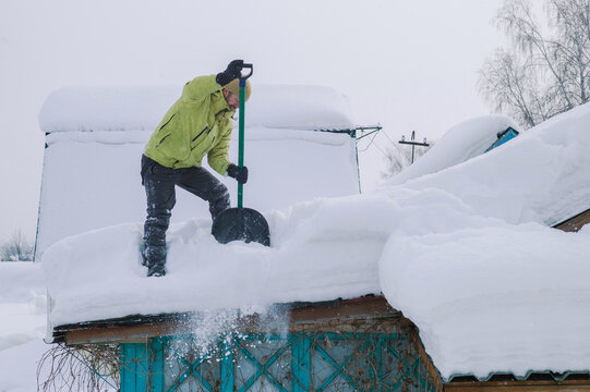 Man in yellow down jacket shovels snow off roof 