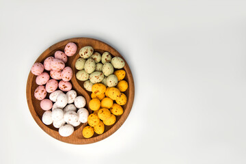 Multi-colored chocolate decorative eggs in wooden plate on a white background. Happy Easter background. Top view