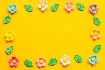 Happy Easter! Stylish colorful flowers flat lay on yellow background. Modern festive template with copy space. Spring composition. Sweet candy flowers and leaves in frame. Greeting card