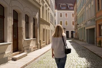 Woman walks along a cozy city street and looks at the architecture. Take a weekend walk in a European city. Leisure and adventure. Beautiful historic architecture. Travel to Europe, tourism. Happy day