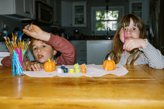 Two children sitting at kitchen table painting pumpkins