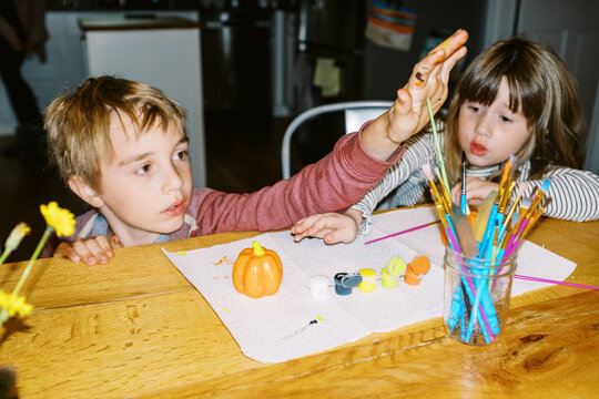 Two children sitting at kitchen table painting pumpkins