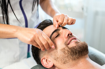 Crop cosmetologist threading male clients eyebrows