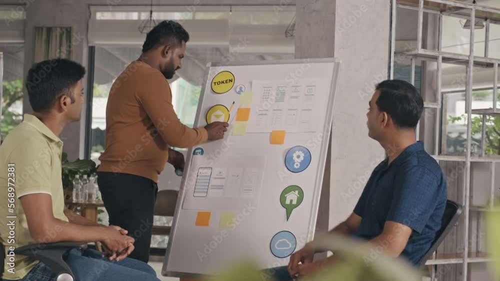 Wall mural indian mobile app developer pointing at icons and sketches on flipchart and giving presentation of s