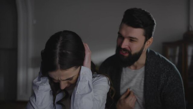 Humiliated woman closes her ears while her husband reproaches and expresses aggression towards her