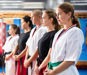 Group of positive females with man trainer posing in gym after karate workout