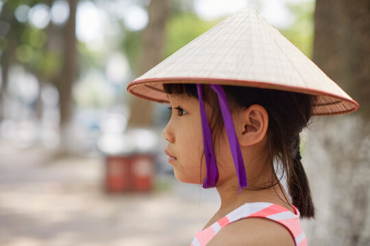 Little Asian girl wearing a Vietnamese straw hat under a big tree 