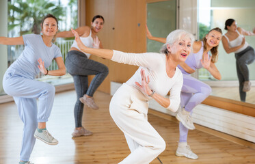 Active positive senior woman performing dance elements during lesson with female group in modern school for adults