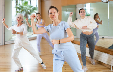 Group of happy young mature sports women in activewear exercising dynamic dancing movemens in modern gym studio