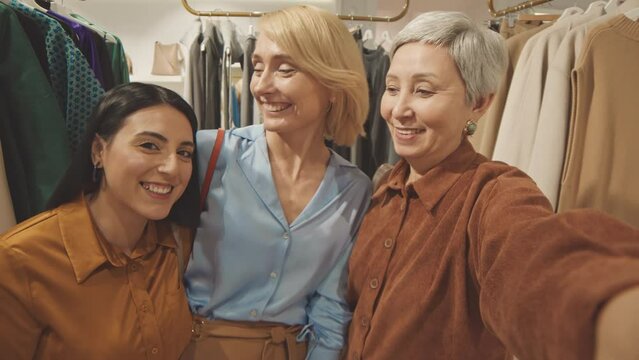 Handheld POV of three happy multiethnic women recording video of themselves shopping together in contemporary clothes store