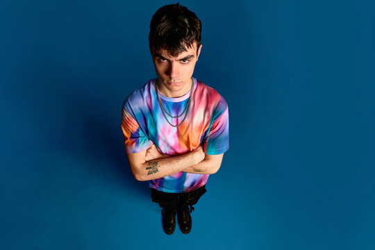 Upset young guy with folded arms in blue studio