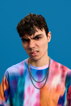 Rebellious young guy making face in blue studio