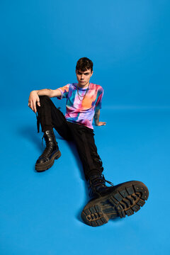 Confident cool guy sitting on floor in blue studio