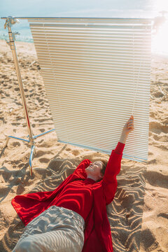 The girl is basking on the beach and manages her comfort with blinds