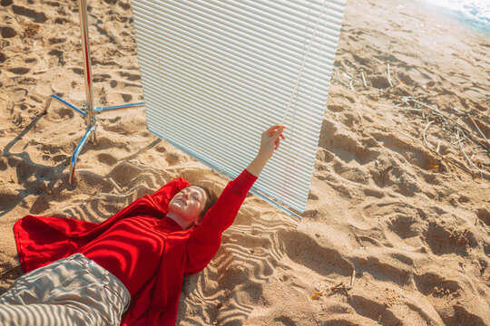 A relaxed girl lies on the sand and adjusts the sunlight blinds